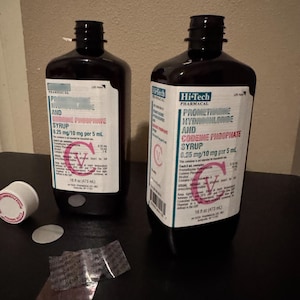 May include: Two dark brown pharmaceutical bottles with white labels, containing Promethazine Hydrochloride and Codeine Phosphate Syrup. The bottles are 16 fl oz (473 ml) each. A small white container and foil packaging are in the foreground.