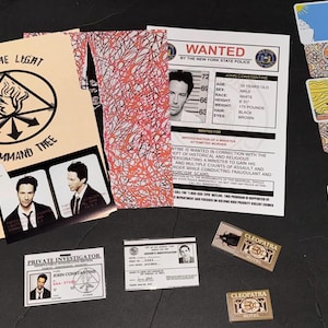 May include: A collection of movie prop replicas including a Wanted poster for John Constantine, a private investigator ID card, a driver's license, two Cleopatra Hotel matchboxes, a business card, and three illustrated tarot cards with a flame symbol.