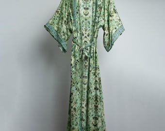 Op de afbeelding: Een lange groene en blauwe geprinte robe met een strikceintuur. De robe heeft een V-hals en lange mouwen.