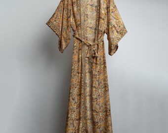 May include: A long, flowing robe with a paisley print in shades of brown, yellow, and blue. The robe has a tie belt and wide sleeves.