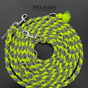 Puede incluir: Una correa para perro trenzada gris y amarillo neón con dos clips plateados y dos anillos plateados. La correa está enrollada y el texto "MILTHOS -handmade- " es visible.