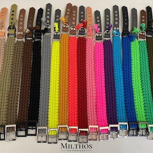 Könnte beinhalten: Eine Auswahl an Hundehalsbändern in verschiedenen Farben, von Beige bis Dunkelgrün. Jedes Halsband hat ein gewebtes Muster und eine Metallschnalle. Die Halsbänder sind in einer Reihe angeordnet, um die Farbpalette zu zeigen. Der Markenname "MILTHOS handmade" ist sichtbar.