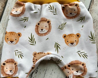 Puede incluir: Pantalones de bebé blancos con un estampado repetido de caras de león de dibujos animados y detalles de hojas verdes. La cintura y los puños son de color amarillo mostaza. Los pantalones son de tela suave.