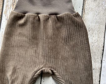 Puede incluir: Pantalones de bebé de pana marrón con cintura alta y textura acanalada. Los pantalones tienen un corte holgado con puños elásticos en los tobillos. La tela parece suave y cómoda, adecuada para bebés y niños pequeños.