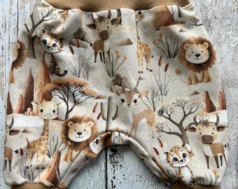 May include: Brown and beige baby pants with a safari animal print. The print features giraffes, lions, zebras, and other animals. The pants have a brown elastic waistband and brown cuffs.