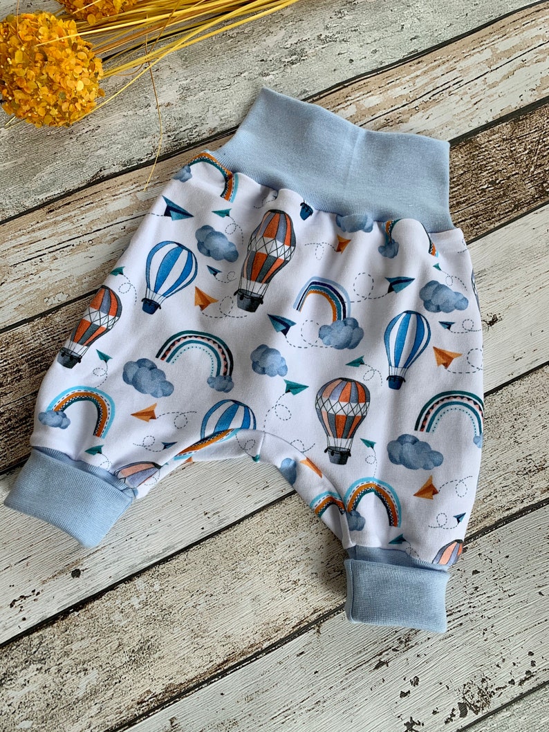 Puede incluir: Pantalones de beb&eacute; blancos con cintura y pu&ntilde;os azules. Los pantalones tienen un estampado colorido de globos aerost&aacute;ticos, arco&iacute;ris y nubes.