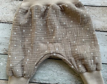 May include: Beige baby pants with a white polka dot pattern. The pants have a wide elastic waistband and cuffed legs.