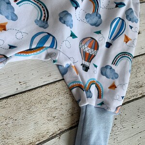 Puede incluir: Pantalones de beb&eacute; blancos con estampado de globo aerost&aacute;tico azul y naranja. Los pantalones tienen un pu&ntilde;o azul en la parte inferior.