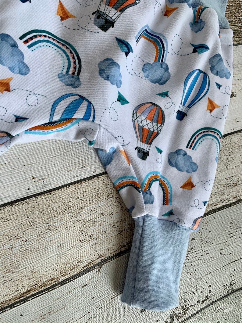 Puede incluir: Pantalones de beb&eacute; blancos con estampado de globo aerost&aacute;tico azul y naranja. Los pantalones tienen un pu&ntilde;o azul en la parte inferior.