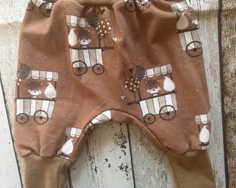 May include: Brown baby pants with a print of bears in a cart with balloons. The pants have a brown elastic waistband and brown cuffs.