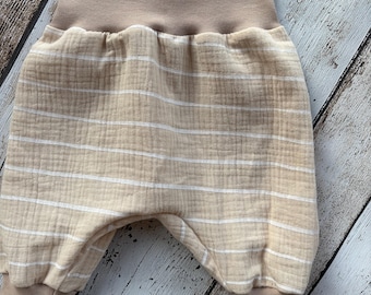 May include: Tan and white striped baby pants with a high waistband and ribbed cuffs. The pants are made of a soft, textured fabric. The overall design is simple and comfortable.