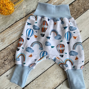 Puede incluir: Pantalones de beb&eacute; blancos con cintura el&aacute;stica y pu&ntilde;os azules. Los pantalones tienen un estampado colorido de globos aerost&aacute;ticos, arco&iacute;ris y nubes.