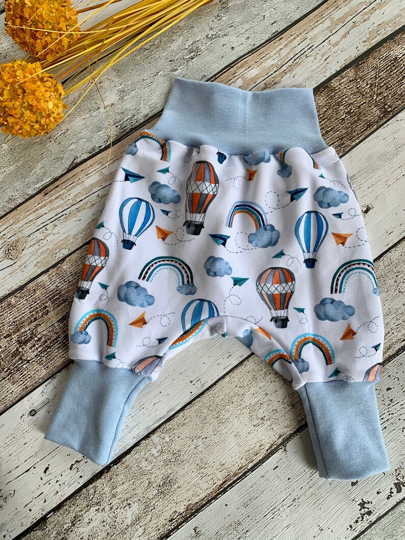 Puede incluir: Pantalones de beb&eacute; blancos con cintura el&aacute;stica y pu&ntilde;os azules. Los pantalones tienen un estampado colorido de globos aerost&aacute;ticos, arco&iacute;ris y nubes.