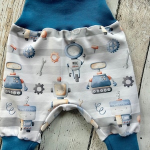 Può includere: Pantaloni da bambino con fascia e polsini blu. I pantaloni presentano un motivo a righe bianche e grigie con robot dei cartoni animati, ingranaggi e chiavi inglesi. I robot sono in tonalità di blu, arancione e grigio.