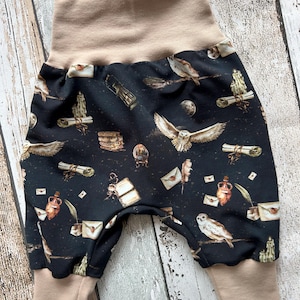 May include: Black and tan baby pants with a print of owls, letters, and other magical objects.