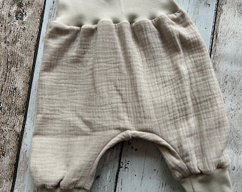 Puede incluir: Pantalones de bebé beige con una cintura elástica ancha y piernas con puños. Los pantalones están hechos de una tela suave y ligera.