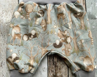 Puede incluir: Pantalones grises para bebé con estampado de animales del bosque que incluye ciervos, ardillas, osos y pájaros sobre un fondo azul claro.