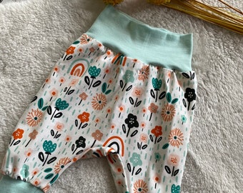 May include: A pair of baby pants with a white background and a colorful floral print. The pants have a light blue elastic waistband and cuffs.