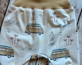 Puede incluir: Pantalones de bebé con cintura y puños color beige. La tela blanca está estampada con un patrón repetido de furgonetas marrones, tablas de surf, palmeras, olas y gaviotas. Los pantalones son de tela suave.