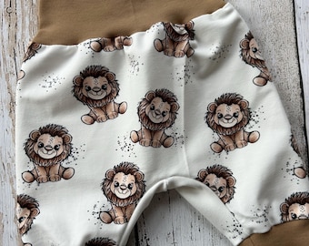 Puede incluir: Pantalones de bebé con un estampado repetido de leones de dibujos animados sobre fondo blanco. La cintura y los puños son marrones. Ropa cómoda para bebés.