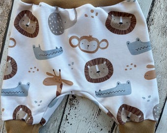Puede incluir: Pantalones de bebé blancos con cintura y puños marrones. Los pantalones tienen un estampado de leones, elefantes, monos, jirafas y cocodrilos de dibujos animados en tonos marrones, grises y azules.