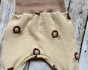 May include: Cream-colored baby pants with a brown lion pattern. The pants have a high, light brown waistband and matching cuffs. The fabric has a textured, crinkled appearance, and the lion illustrations are evenly spaced.