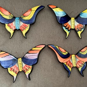 May include: Four colourful ceramic butterfly wall decorations. Each butterfly has a different colour scheme, including blue, yellow, orange, and red.