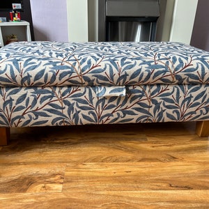 May include: A blue and white floral patterned storage ottoman with a wooden frame and legs. The ottoman has a hinged lid and a pull tab for opening.