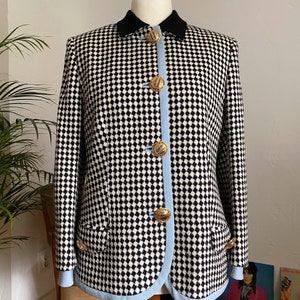 May include: A black and white checked blazer with a blue trim and gold buttons. The blazer has a black collar and a single pocket on the left side.