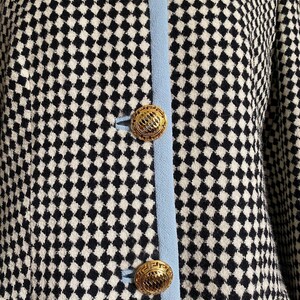 May include: A black and white checked jacket with a blue trim and gold buttons. The buttons have a geometric design.