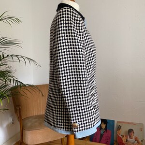 May include: A black and white checked blazer with a blue trim and a gold button. The blazer is on a mannequin.