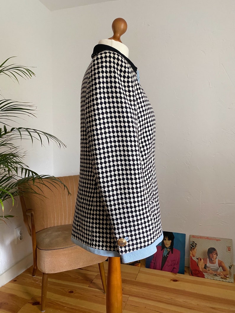May include: A black and white checked blazer with a blue trim and a gold button. The blazer is on a mannequin.