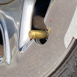 May include: A close-up of a silver car wheel with a brass bullet used as a valve stem cap.