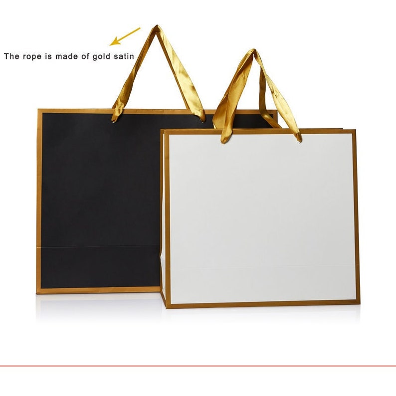 May include: Two paper gift bags with gold ribbon handles. One bag is black with a gold trim and the other is white with a gold trim.