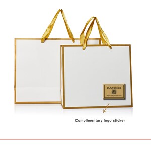 May include: Two white gift bags with gold trim and yellow ribbon handles. The bag on the right has a brown logo sticker with the text "DLKJ-Studio" and a website address.