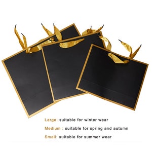 May include: Three black gift bags with gold trim and gold ribbon handles. The bags are arranged in a stack, with the largest bag on the bottom and the smallest bag on top. The text on the image reads: "Large: suitable for winter wear", "Medium: suitable for spring and autumn", and "Small: suitable for summer wear".