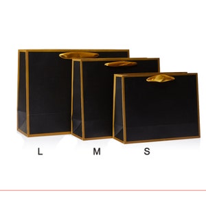 May include: Three black gift bags with gold trim and ribbon handles. The bags are labeled L, M, and S.