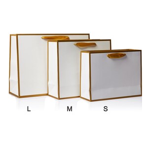 May include: Three white gift bags with gold trim and ribbon handles. The bags are labeled L, M, and S.