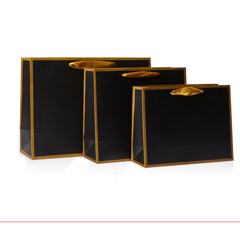 May include: Three black gift bags with gold trim and gold ribbon handles. The bags are arranged in descending size order.