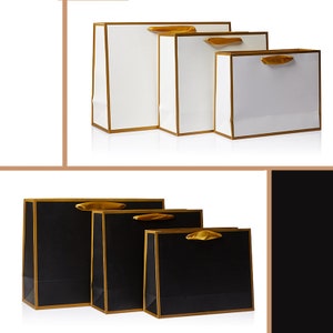 May include: Three different sizes of gift bags with gold trim and handles. The bags are white with gold trim and handles. The bags are arranged in order of size, with the largest bag on the left and the smallest bag on the right.