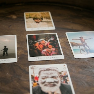 May include: Five tarot cards laid out on a wooden surface. The cards are white with black text and feature images of people in various settings. The cards are: Six of Swords, The Empress, The Sun, The Tower, and The World.