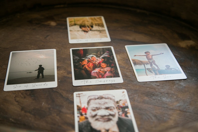 May include: Five tarot cards laid out on a wooden surface. The cards are white with black text and feature images of people in various settings. The cards are: Six of Swords, The Empress, The Sun, The Tower, and The World.
