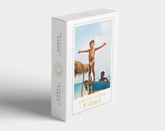Könnte beinhalten: Eine weiße Schachtel mit einem goldenen Foliendesign. Die Schachtel zeigt ein Foto von zwei Kindern auf einem Boot, mit dem Text "The Gift of Life Tarot" auf der Vorderseite.