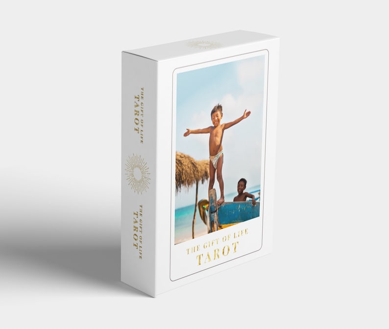 May include: A white box with a gold foil design. The box features a photo of two children on a boat, with the text "The Gift of Life Tarot" printed on the front.