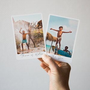 May include: Two Polaroid-style photos with handwritten text. The first photo shows two children playing in a water spray. The text below the photo reads "Three of Water". The second photo shows a child standing on a boat with arms outstretched. The text below the photo reads "The Sun".