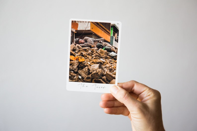 May include: A black and white photo of a man lying on a pile of rubble. The photo is titled "The Tower".