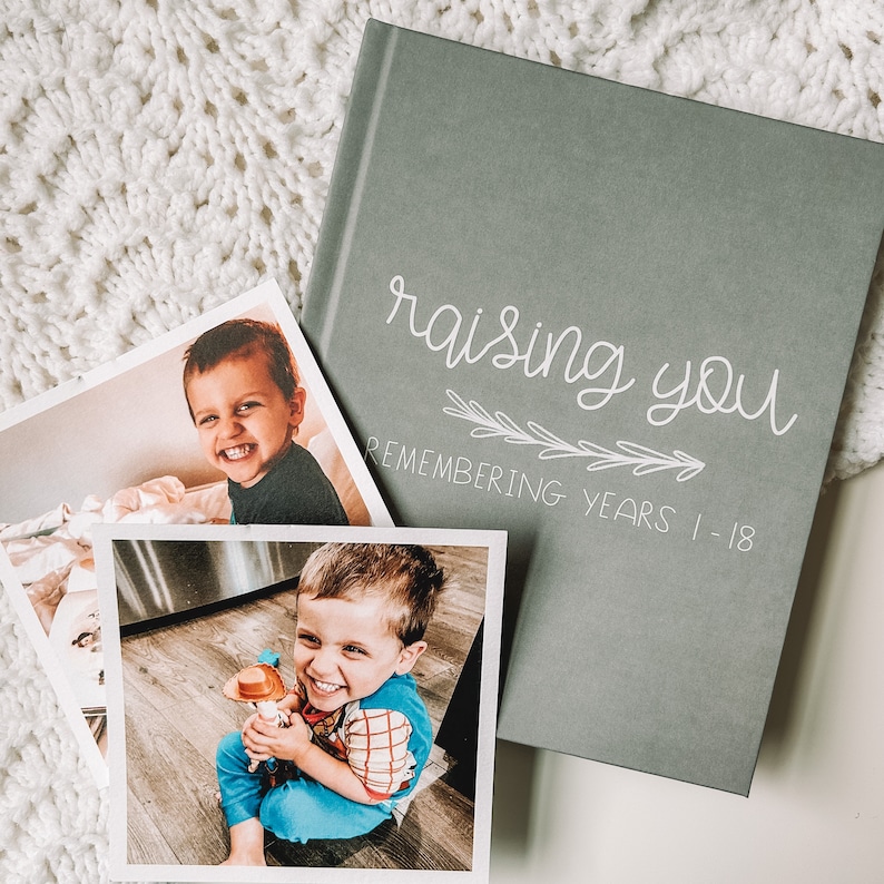 Grey childhood memory book titled Raising You Remembering Years 1-18 in white text.