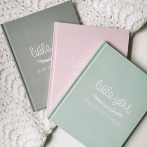 The baby book is available in three colors which are grey, blush pink, and sage green. All feature the title of the book, Little You Babys First Year, printed in white ink.