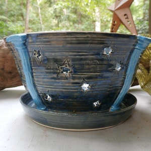 May include: A dark blue ceramic planter with a glossy finish and horizontal textured lines. The bowl features cut-out star shapes and three vertical light blue decorative ribs extending from the rim to the base, resting on a matching saucer.