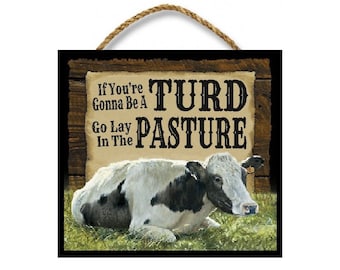 Puede incluir: Un letrero de madera con una vaca acostada en un campo de hierba. El letrero dice "If You're Gonna Be A Turd Go Lay In The Pasture".
